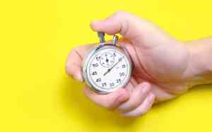 Hand holds stopwatch in front of yellow background